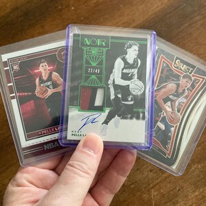 May include: Three basketball trading cards featuring Miami Heat player Pelle Larsson. The center card is a Noir edition, numbered 22/49, with a patch and signature. The other cards show Larsson in action, with the Miami Heat logo visible.