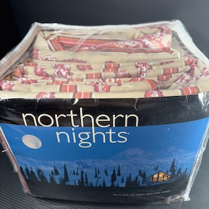 May include: A folded bedding set in a clear plastic package labeled Northern Nights. The fabric features a tan background with a repeating pattern of red and white floral motifs and horizontal stripes. The packaging includes a mountain landscape.