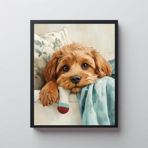 Pode incluir: Impressão emoldurada de um cão castanho com grandes olhos castanhos, repousando sobre uma superfície branca com um cobertor azul e uma almofada floral. O cão está segurando uma meia na boca. A obra de arte tem um estilo suave e pictórico.