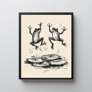 May include: Black and white illustration of two frogs jumping above lily pads. The frogs are depicted with their arms raised, and the artwork has a vintage, hand-drawn style. The image is framed in a black border.