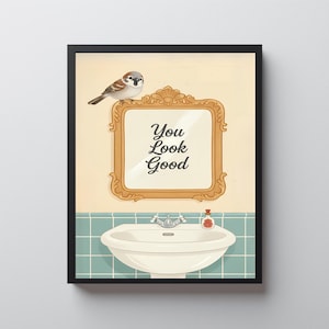 Puede incluir: Impresión artística enmarcada que muestra un gorrión sobre un espejo dorado con el texto "You Look Good". Debajo hay un lavabo blanco y una botella pequeña.