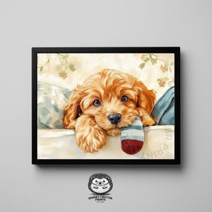 May include: A framed print of a golden-brown puppy resting on a bed, holding a striped sock in its mouth. The artwork has a soft, painterly style with floral accents and a black frame. The print is from Quirky Critter Prints.