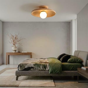 Può includere: Una plafoniera circolare a incasso caratterizzata da un ampio paralume a disco in legno chiaro con una lampadina sferica centrale in vetro bianco che emette una luce calda e soffusa, montata direttamente al soffitto.