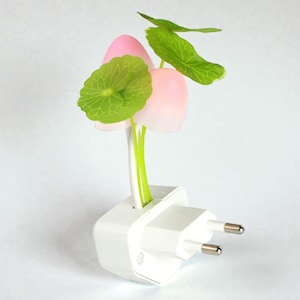 May include: A mushroom-shaped night light with pink caps and green leaves, designed to plug into a white wall socket. The stems are green, and the leaves are a vibrant green. A decorative and functional item.