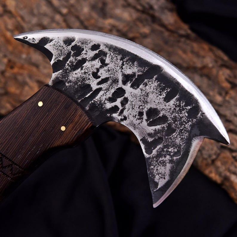 Peut inclure: Une hache artisanale &agrave; lame incurv&eacute;e et manche en bois fonc&eacute;. La t&ecirc;te de la hache pr&eacute;sente un motif textur&eacute; et mouchet&eacute;, fix&eacute;e au manche par des rivets en laiton. La lame est tranchante et incurv&eacute;e, con&ccedil;ue pour couper ou hacher.