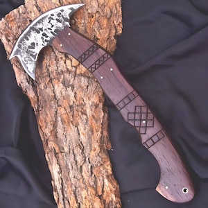 Peut inclure: Une hache artisanale avec une lame en acier incurv&eacute;e et textur&eacute;e et un manche en bois fonc&eacute;. Le manche pr&eacute;sente des motifs d&eacute;coratifs grav&eacute;s et est mont&eacute; sur un morceau de bois textur&eacute;. La hache est con&ccedil;ue pour l'utilit&eacute; et l'exposition.