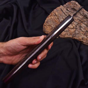 Peut inclure: Un couteau artisanal avec un manche en bois fonc&eacute; et une lame argent&eacute;e. Le manche pr&eacute;sente un motif textur&eacute; et un accent argent&eacute;. Le couteau est pr&eacute;sent&eacute; sur un fond sombre, mettant en valeur son design et son savoir-faire.