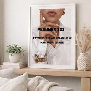 Puede incluir: Impresión artística enmarcada con el texto "PSAUMES 23:1" y texto en francés. La imagen muestra a una persona con una camisa blanca y un reloj dorado. La obra de arte se exhibe en una estantería de madera.
