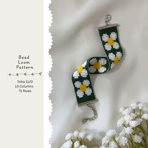 Op de afbeelding: Een kralen geweven armband met een madeliefjespatroon. De armband heeft witte madeliefjes met gele centra op een donkergroene achtergrond. Het heeft zilverkleurige metalen sluitingen en een ketting voor aanpassing. De tekst links luidt "Bead Loom Pattern".