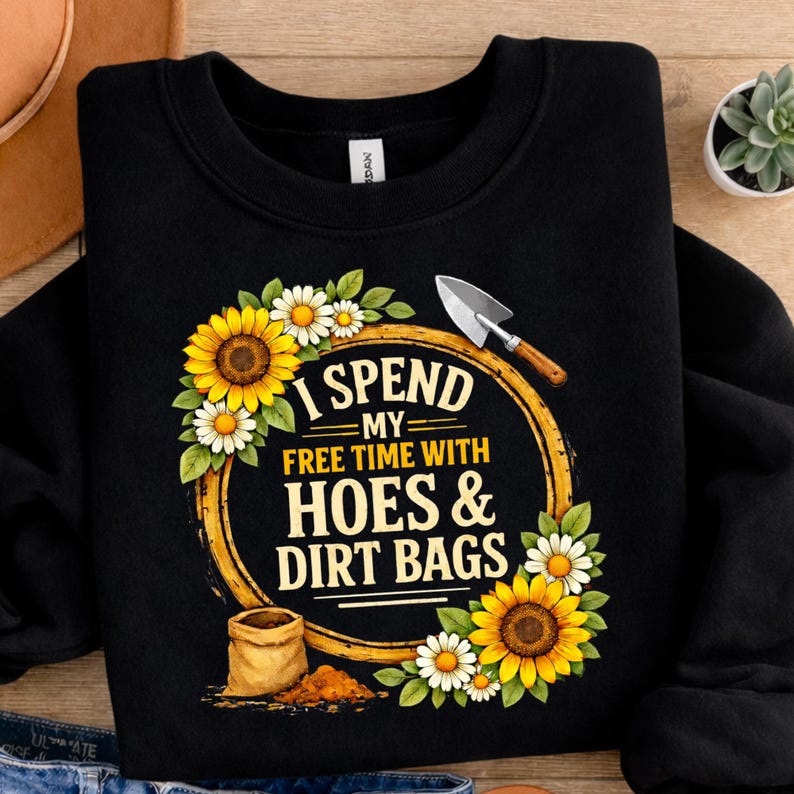 May include: Black sweatshirt with a gardening-themed graphic. The design features sunflowers, daisies, and the text "I Spend My Free Time With Hoes & Dirt Bags." A trowel and a bag of dirt are also included.