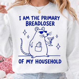 Könnte beinhalten: Ein weißes Sweatshirt mit Rundhalsausschnitt und einer blauen Grafik einer Ratte mit Sonnenbrille, die ein Martiniglas und ein Stück Brot in einer Tasche hält. Der Text lautet I AM THE PRIMARY BREADLOSER OF MY HOUSEHOLD in blauen Buchstaben.