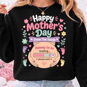 Può includere: Felpa nera con grafica colorata per la festa della mamma. Il design include il testo "Happy Mother's Day" e "From The Inside". Una grafica di pancia incinta mostra una barra di caricamento con il testo "Mommy-to-be loading..." e "please wait."