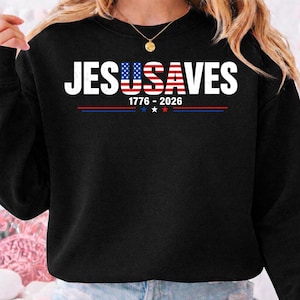 May include: A black long-sleeve sweatshirt featuring the white text JESUSAVES with the letters USA stylized as an American flag. Below the text, the numbers 1776-2026 are printed in white, followed by a horizontal line with three small stars.