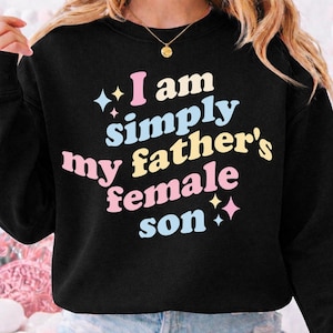 Può includere: Una felpa nera a maniche lunghe con il testo "I am simply my father's female son" stampato in un carattere in stile retrò multicolore. Le lettere utilizzano tonalità azzurro, giallo pallido e rosa tenue, accentuate da piccole icone a forma di stella.
