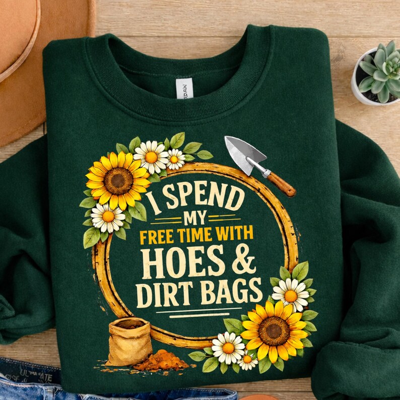 May include: Dark green sweatshirt with the text "I SPEND MY FREE TIME WITH HOES & DIRT BAGS" surrounded by sunflowers, daisies, and a trowel. A small bag of dirt is also featured in the design.