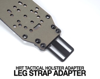 May include: An olive drab tactical holster adapter featuring a rigid panel with multiple circular mounting holes and a black metal attachment point secured by four screws. The text HRT TACTICAL HOLSTER ADAPTER LEG STRAP ADAPTER is printed in bold black letters below the object.