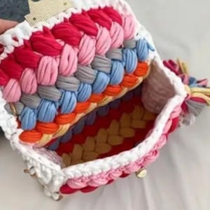 May include: A handmade, open handbag with a colorful, braided design. The bag features a white border and a variety of colors, including red, pink, gray, blue, orange, and yellow. The interior is visible, showcasing a matching color scheme.