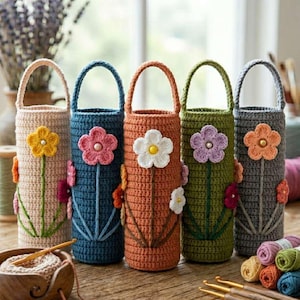 May include: Five colorful, crocheted bottle holders with flower designs. Each holder features a different color: beige, blue, orange, green, and gray. The flower accents include yellow, pink, white, purple, and orange. The holders have a handle at the top and are displayed on a wooden surface.