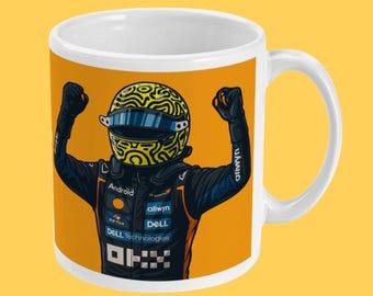 May include: White ceramic mug featuring a vibrant illustration of a race car driver in a helmet with a yellow and black design, arms raised in victory. The mug has a bright orange background.