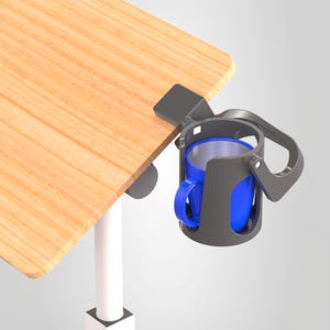 Puede incluir: Un portavasos de plástico gris oscuro sujeto al borde de un escritorio con veta de madera clara. El soporte cuenta con un marco circular con un asa lateral y contiene una taza azul brillante con un revestimiento interior plateado.