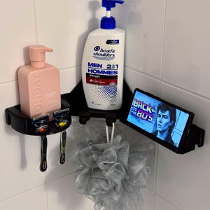 Könnte beinhalten: Ein schwarzer Eck-Dusch-Organizer mit einer rosa Shampooflasche, zwei Rasierern und einer Head & Shoulders-Flasche. Ein Tablet mit der Aufschrift "BACK TO THE 80'S" ist rechts montiert. Ein grauer Luffa hängt darunter.