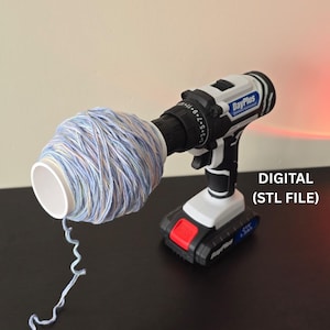 Op de afbeelding: Een wit en zwarte snoerloze boormachine houdt een spoel blauw en wit garen vast. De boormachine staat op een donkere ondergrond. De tekst "DIGITAL (STL FILE)" is zichtbaar. Voor handwerk.