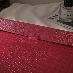 Puede incluir: Una funda roja para port&aacute;til con efecto piel de cocodrilo y cierre de solapa. La funda es de un tono rojo intenso y tiene una superficie texturizada. La solapa se asegura con una peque&ntilde;a leng&uuml;eta. La funda est&aacute; dise&ntilde;ada para proteger un port&aacute;til o una tableta.