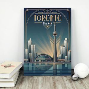 May include: Art Deco style Toronto poster featuring the CN Tower, city skyline, and the text "TORONTO The 6IX" in gold lettering against a teal and blue background. The poster is displayed on a white wall.