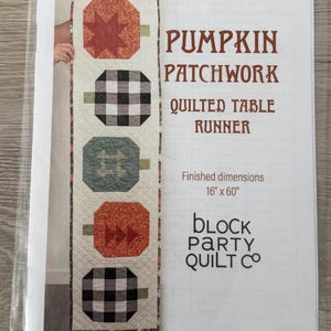 May include: A sewing pattern for a Pumpkin Patchwork Quilted Table Runner by Block Party Quilt Co. The cover shows a vertical runner with five pumpkin blocks in orange, black and white plaid, and sage green. Finished dimensions are 16 inches by 60 inches.