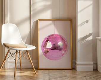 Puede incluir: Una impresión enmarcada con una bola de discoteca rosa. La bola está cubierta de pequeños cuadrados reflectantes. La impresión está en un marco dorado y cuelga sobre un fondo rosa claro. Una silla blanca con patas de madera está en primer plano.