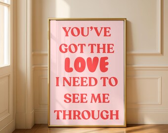 Puede incluir: Una lámina de arte mural rectangular en un marco dorado con fondo rosa claro y texto rojo en negrita que dice: YOU'VE GOT THE LOVE I NEED TO SEE ME THROUGH. La tipografía está centrada y utiliza una mezcla de fuentes serif y redondeadas.