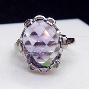 May include: A silver ring with a large, clear, faceted gemstone. The ring has a delicate, ornate design.