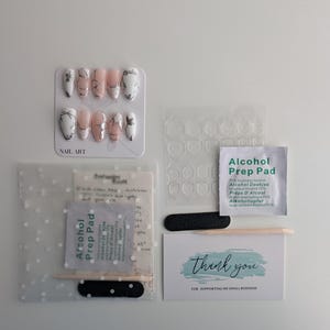 Puede incluir: Un kit de arte de u&ntilde;as con u&ntilde;as postizas, pesta&ntilde;as adhesivas para u&ntilde;as, almohadillas con alcohol, limas de u&ntilde;as y una tarjeta de agradecimiento. Las u&ntilde;as postizas presentan un dise&ntilde;o de m&aacute;rmol con detalles en blanco y negro.