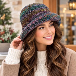 Può includere: Un cappello a secchiello all'uncinetto caratterizzato da un motivo in filato variegato con toni misti di verde scuro, viola, blu e oro. Il cappello presenta una corona arrotondata e una tesa spiovente, realizzata con un punto spesso e strutturato.