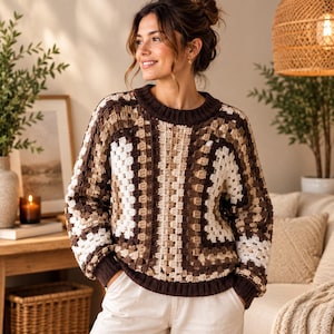 May include: A long-sleeve crochet sweater featuring a granny square pattern in shades of dark brown, light brown, and cream. The garment has a ribbed crew neckline, ribbed cuffs, and a ribbed hem, all in a solid dark brown yarn color.