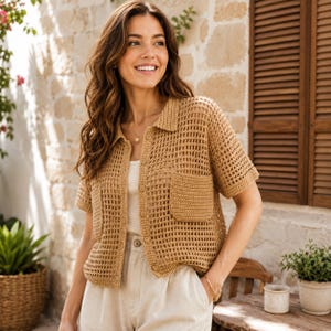 May include: A tan crochet button-down shirt featuring a loose, open-knit mesh pattern, a classic collar, short sleeves, and two square patch pockets on the front. The garment is worn over a plain white top and paired with light-colored trousers.