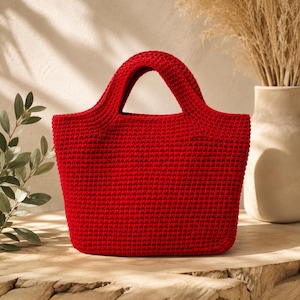 May include: A vibrant red handbag featuring a dense, uniform crochet stitch pattern. The bag has a structured, trapezoidal silhouette with two integrated, rounded handles at the top, providing a consistent texture throughout the entire exterior.
