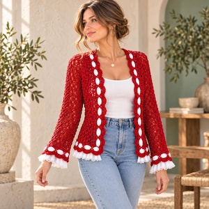 May include: A red crochet cardigan featuring an open-knit pattern, long sleeves, and a white scalloped trim along the front opening and cuffs. The garment is worn over a plain white tank top and light blue denim jeans.