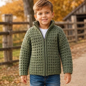Puede incluir: Una chaqueta de manga larga color verde salvia con cremallera, un patrón de tejido de punto gofrado, cuello alto y cremallera frontal completa, sobre una camiseta blanca lisa y pantalones vaqueros azules.