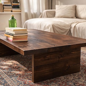 Peut inclure: Une table basse rectangulaire en bois brun foncé avec une pile de livres et une bouteille verte dessus. La table est faite de planches épaisses et repose sur un tapis à motifs. La table mesure environ 152 cm de long.