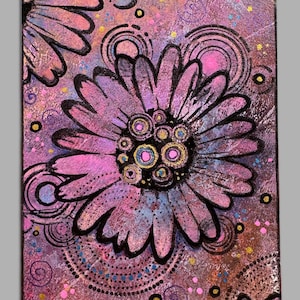 May include: A rectangular art piece featuring a large, central pink and purple flower with black outlines. The background is a textured mix of purple, pink, and brown tones, decorated with black circular patterns, swirls, and small yellow and pink dots.