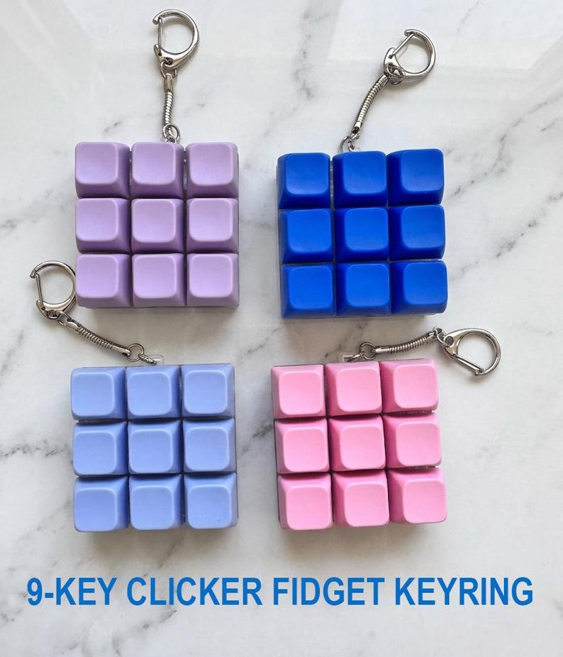 May include: Four square 9-key clicker fidget keyrings in lavender, blue, periwinkle, and pink. Each keyring features a grid of nine square buttons attached to a silver metal split ring by a short chain. The text 9-KEY CLICKER FIDGET KEYRING is visible.