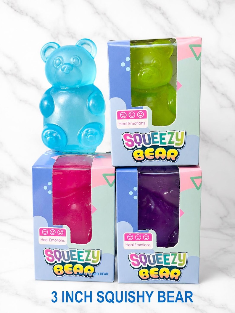 May include: A blue translucent bear-shaped toy stands next to three rectangular boxes labeled SQUEEZY BEAR and Heal Emotions. The boxes contain green, pink, and purple bear-shaped toys. The text 3 INCH SQUISHY BEAR is printed at the bottom.