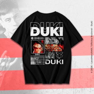 May include: Black t-shirt featuring the word "DUKI" in large white block letters. The shirt includes images of a person, a Spotify logo, and the words "POPULAR RELEASES". The design incorporates a wing graphic and the artist's name.