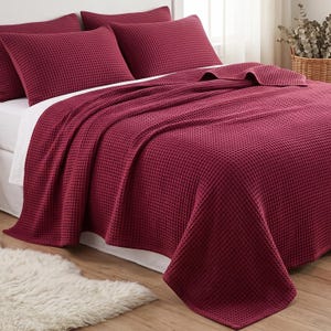 Può includere: Un copriletto color bordeaux intenso con trama a nido d'ape e due federe abbinate su un letto con lenzuola bianche. La biancheria da letto presenta una distinta trama a griglia su tutti gli elementi, creando un aspetto uniforme.