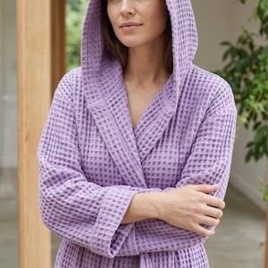 Peut inclure: Un peignoir à capuche en tissu gaufré de couleur lilas. Le peignoir est doté d'un col châle et d'une capuche assortie. Le tissu présente un motif texturé en forme de grille. Le peignoir est conçu pour le confort et la détente.