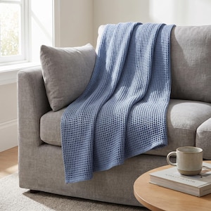 Peut inclure: Un jeté de lit bleu pervenche avec une texture gaufrée distincte drapé sur un canapé gris. La couverture présente un motif en forme de grille créé par les carrés de tissu en relief, offrant une surface uniforme et tactile sur toute la pièce.