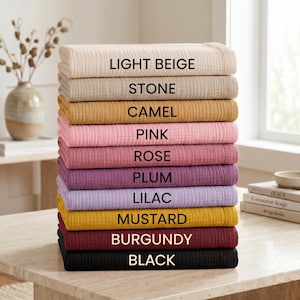 May include: A stack of ten folded fabric items in various colors, including light beige, stone, camel, pink, rose, plum, lilac, mustard, burgundy, and black. Each item has a textured, ribbed appearance, with the color names printed on each item.