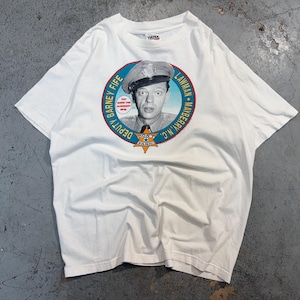 Può includere: T-shirt bianca con grafica circolare di Barney Fife di The Andy Griffith Show. La grafica include il testo "Deputy Barney Fife, Lawman, Mayberry, N.C." e "Don't Panic". La maglietta è realizzata in materiale morbido.