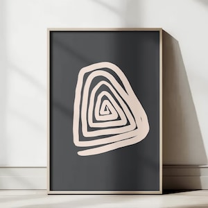May include: Framed abstract art print featuring a light beige spiral design on a dark gray background. The artwork is displayed in a wooden frame and leans against a white wall and floor, creating a minimalist aesthetic.